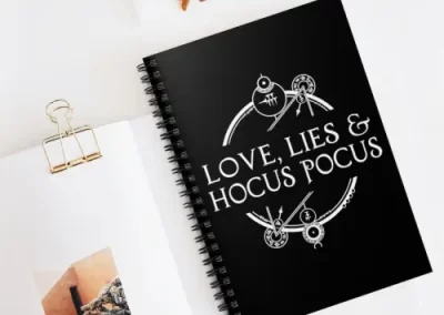 A picture of a notebook with the Love, Lies, and Hocus Pocus logo printed on it.